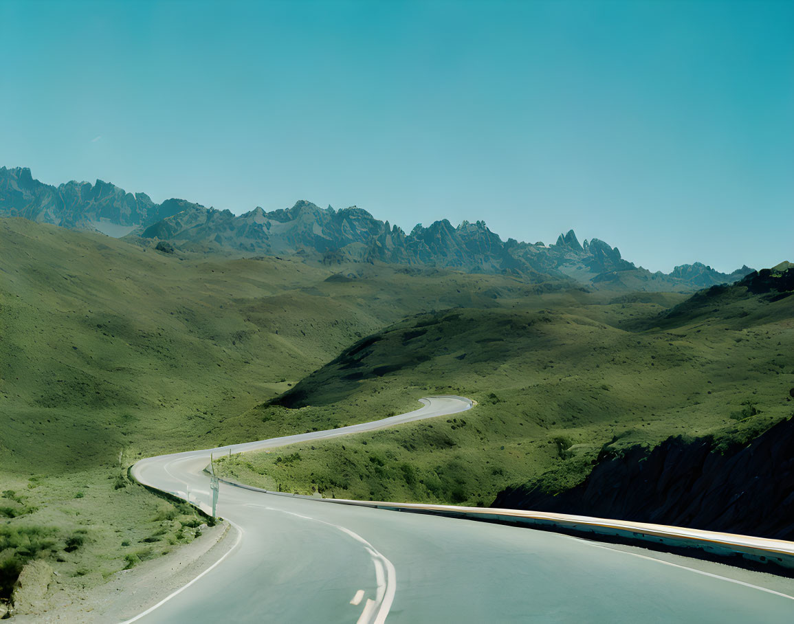 Curving road in green landscape with mountain peaks under blue sky