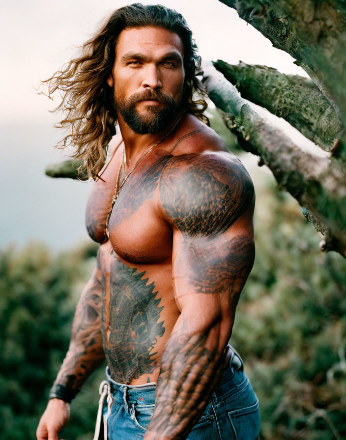 Muscular man with full-body tattoos in jeans against natural backdrop