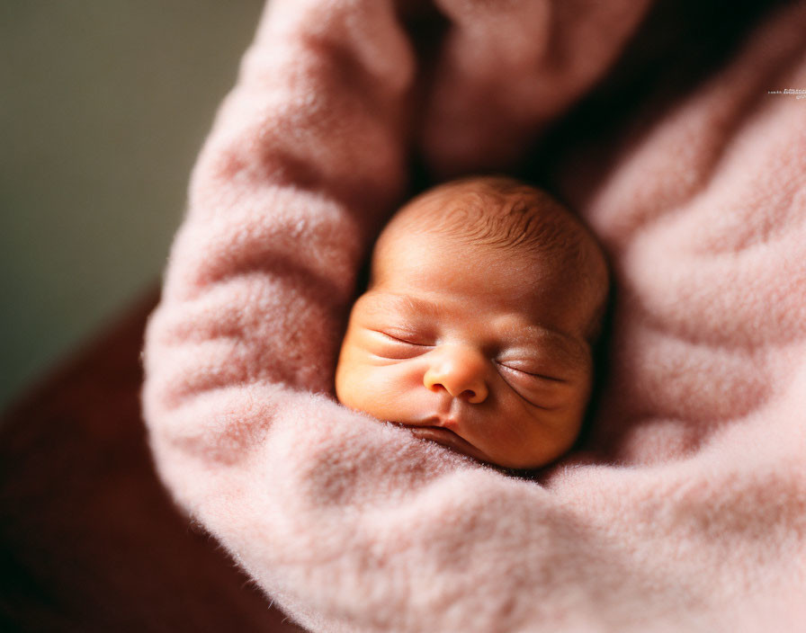 Newborn baby sleeping in soft pink blanket with gentle light glow