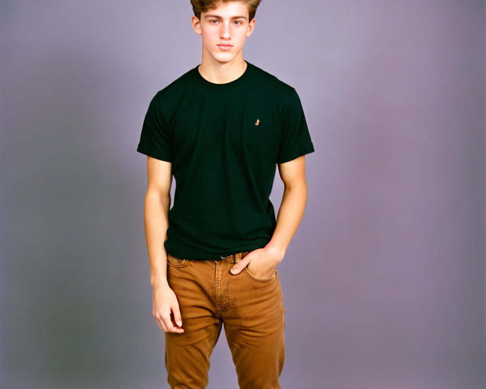 Young man in black t-shirt and brown trousers against gray background