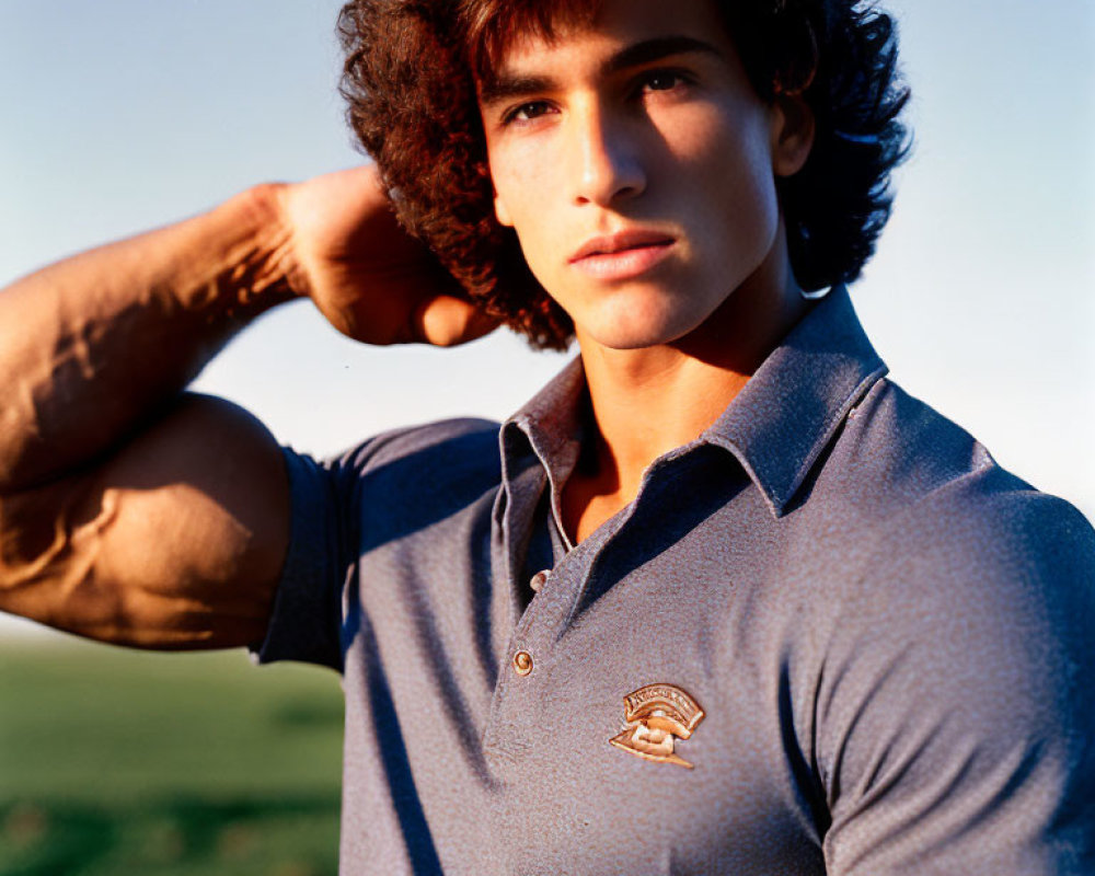 Curly-Haired Young Man in Blue Polo Shirt Poses in Field at Sunset