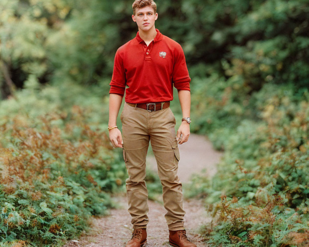 Young man in red polo shirt and khaki pants on forest trail gazes at camera