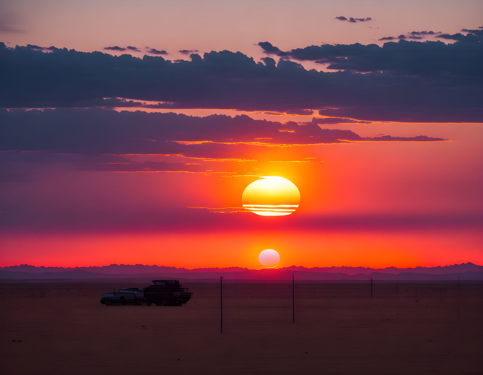 Vibrant orange and pink sunset over desert landscape with vehicle silhouette