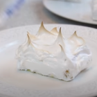 Lemon cheesecake with whipped cream on white plate, water glass & slice in background