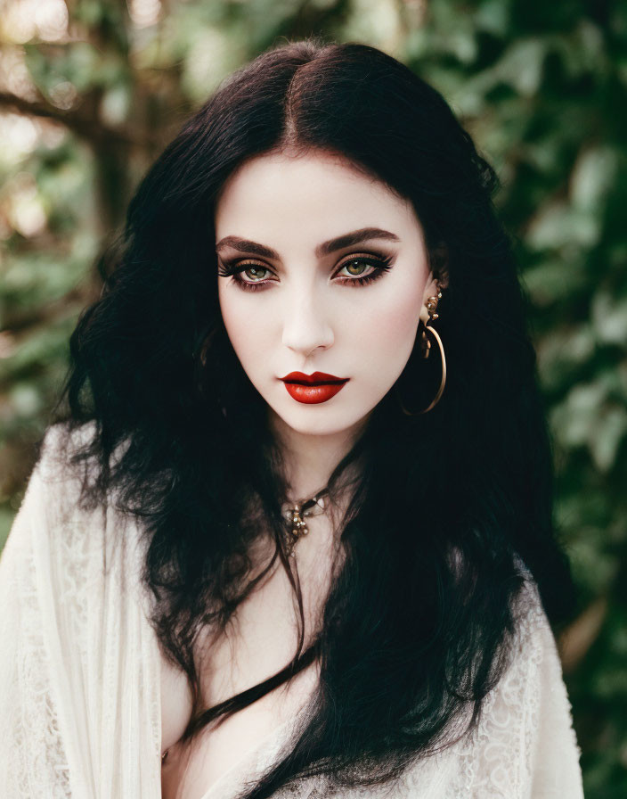 Dark-haired woman in white outfit with red lipstick and gold earrings against green backdrop