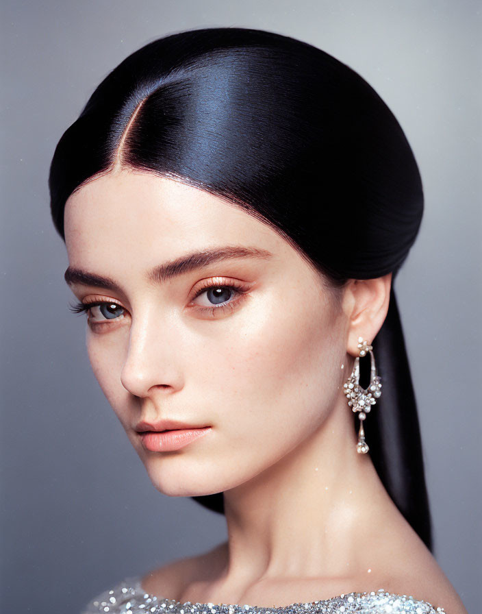 Woman with Sleek Bun Hairstyle and Sparkling Earring in Silver Dress