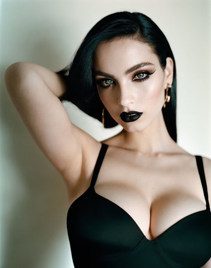 Dark-haired woman in striking makeup and black outfit posing with hand behind head