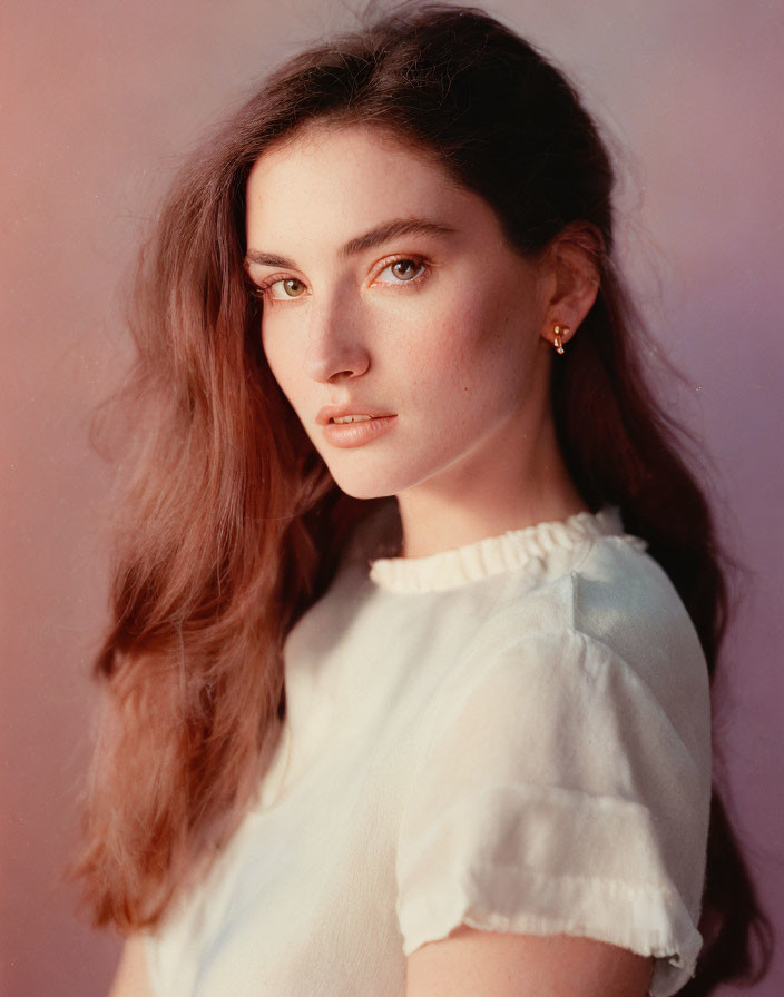 Young woman with long brown hair in white blouse gazes at camera.