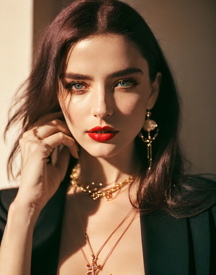 Portrait of a woman with dark hair, green eyes, red lipstick, and gold jewelry in sunlight.