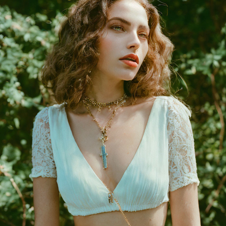 Curly-haired woman in blue top with layered necklaces against green backdrop