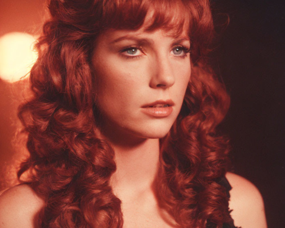 Curly Red-Haired Woman in Black Outfit Against Warm Background