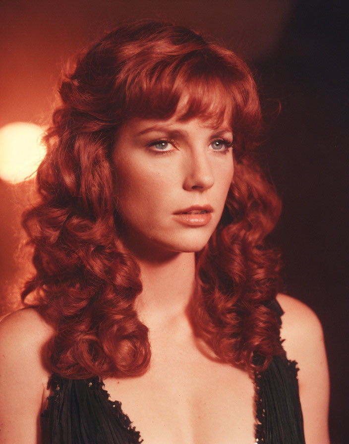 Curly Red-Haired Woman in Black Outfit Against Warm Background