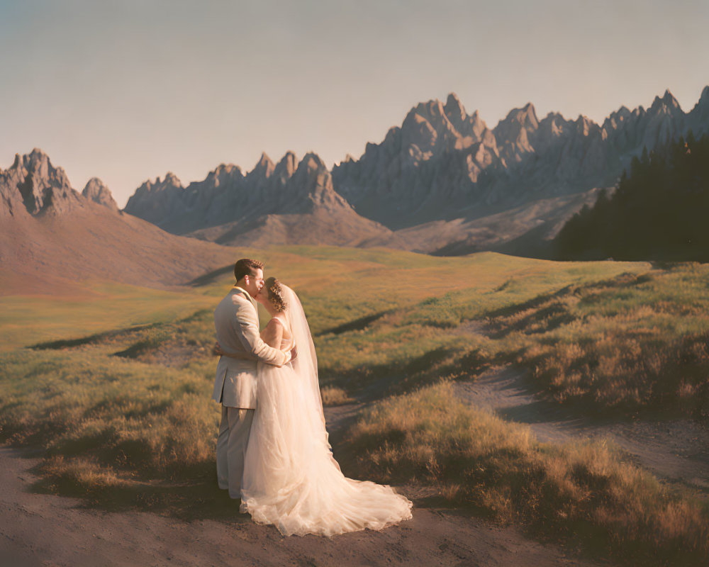 Bride and groom embrace in serene meadow with dramatic mountain peaks.