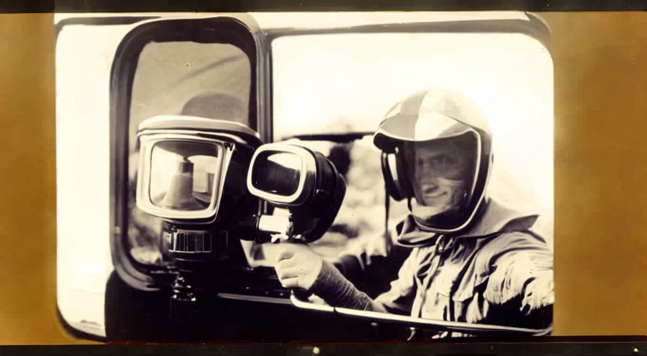 Smiling person in vintage photo with helmet pointing in race car