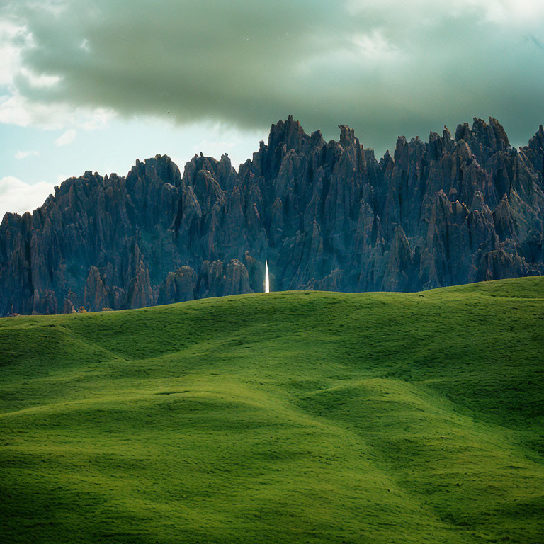 Scenic landscape: green hill and rocky mountains under cloudy sky