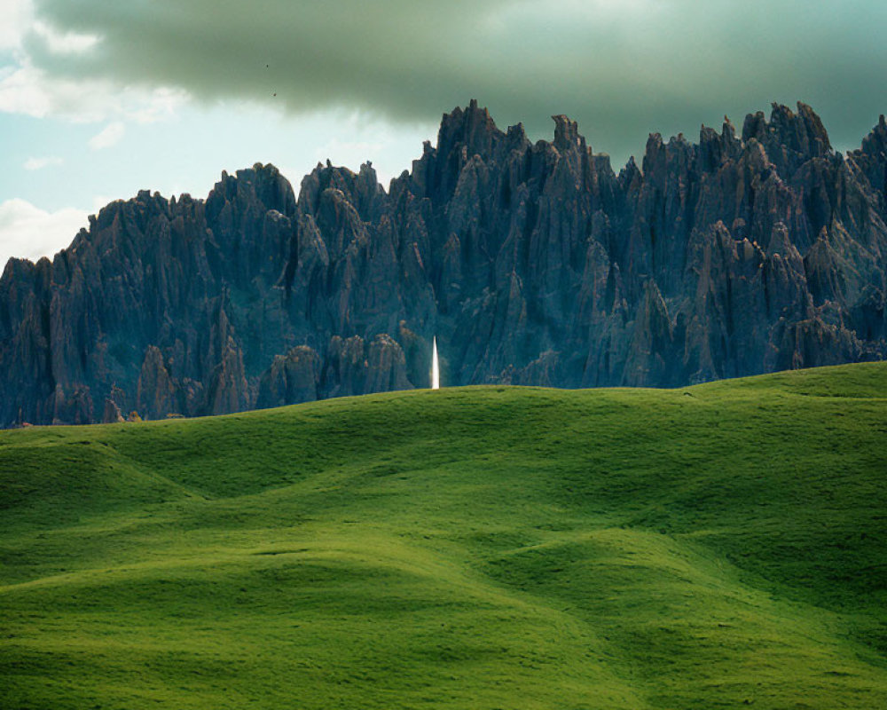 Scenic landscape: green hill and rocky mountains under cloudy sky