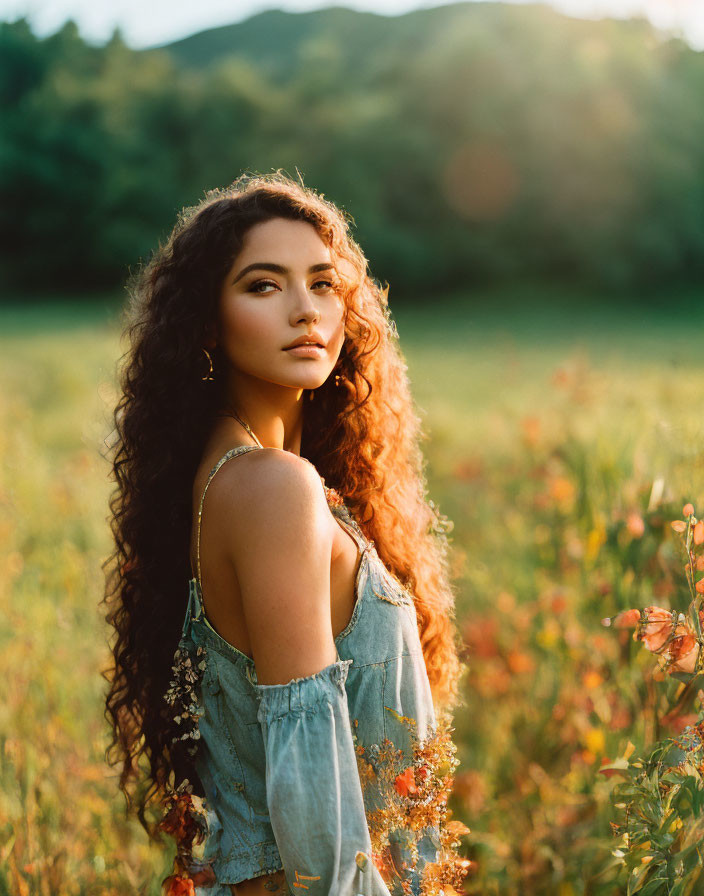 Curly-haired woman in denim top standing in sunlit flower field