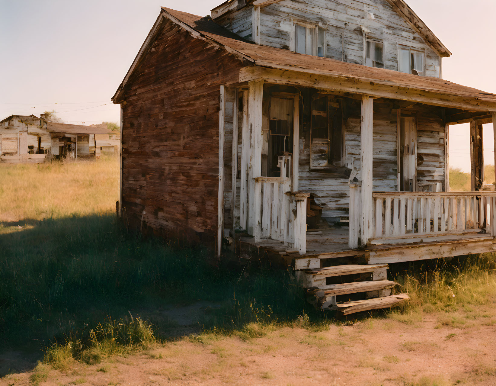 Weathered wooden house with porch and missing planks in grassy field