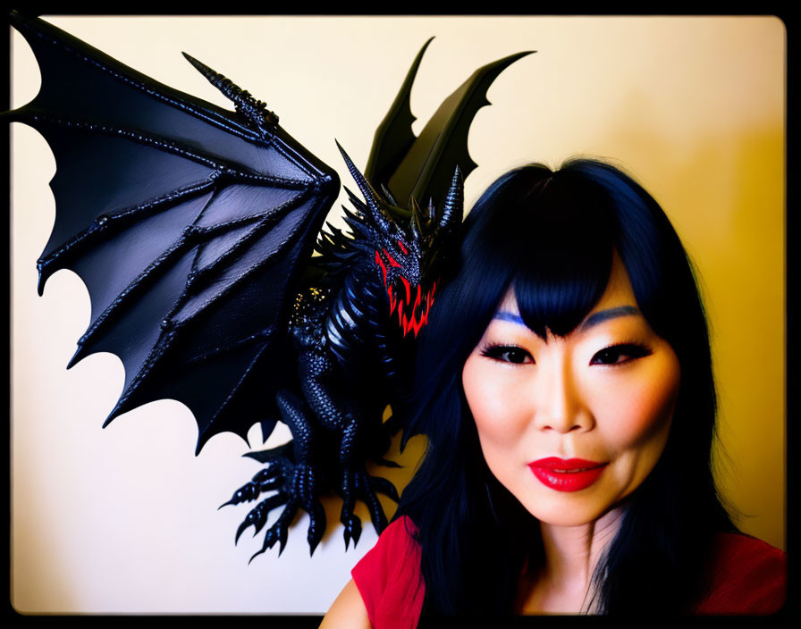 Dark-haired woman poses with black dragon model featuring red eyes and wings.