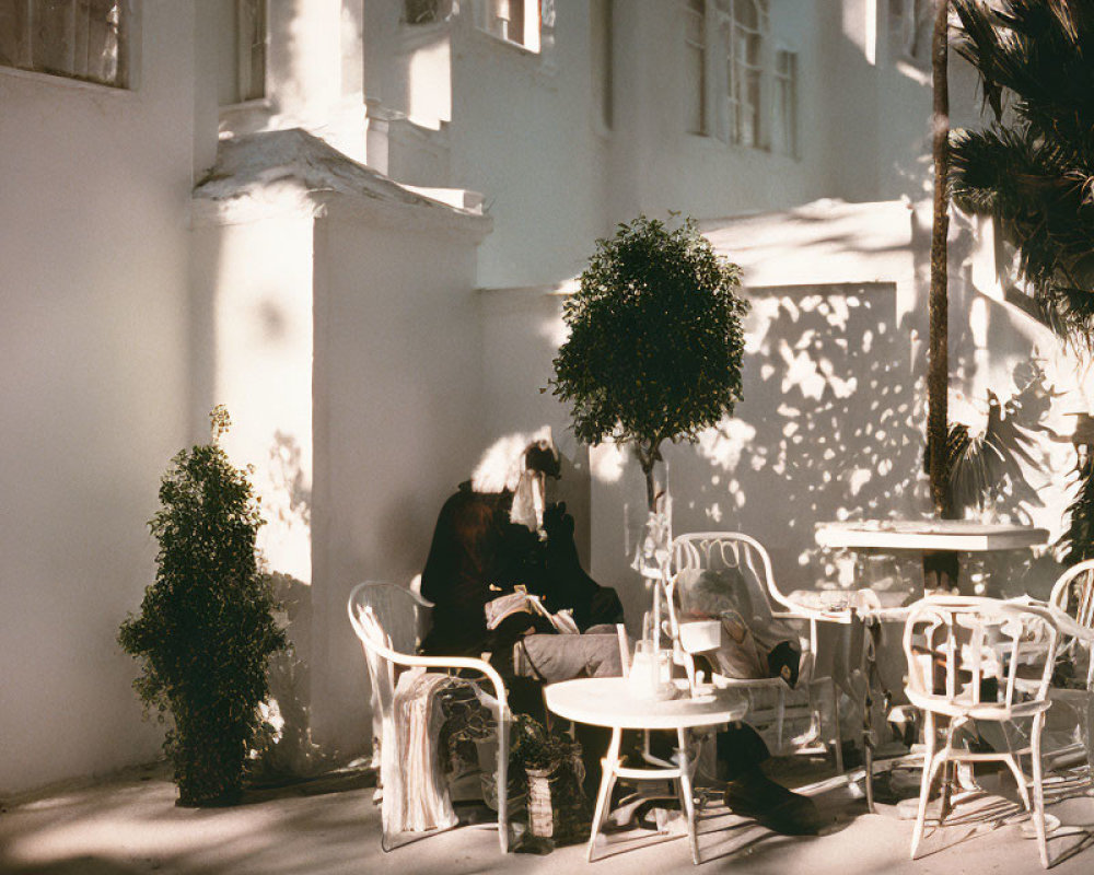 Person at Cafe Table in Shadow-Patterned Courtyard