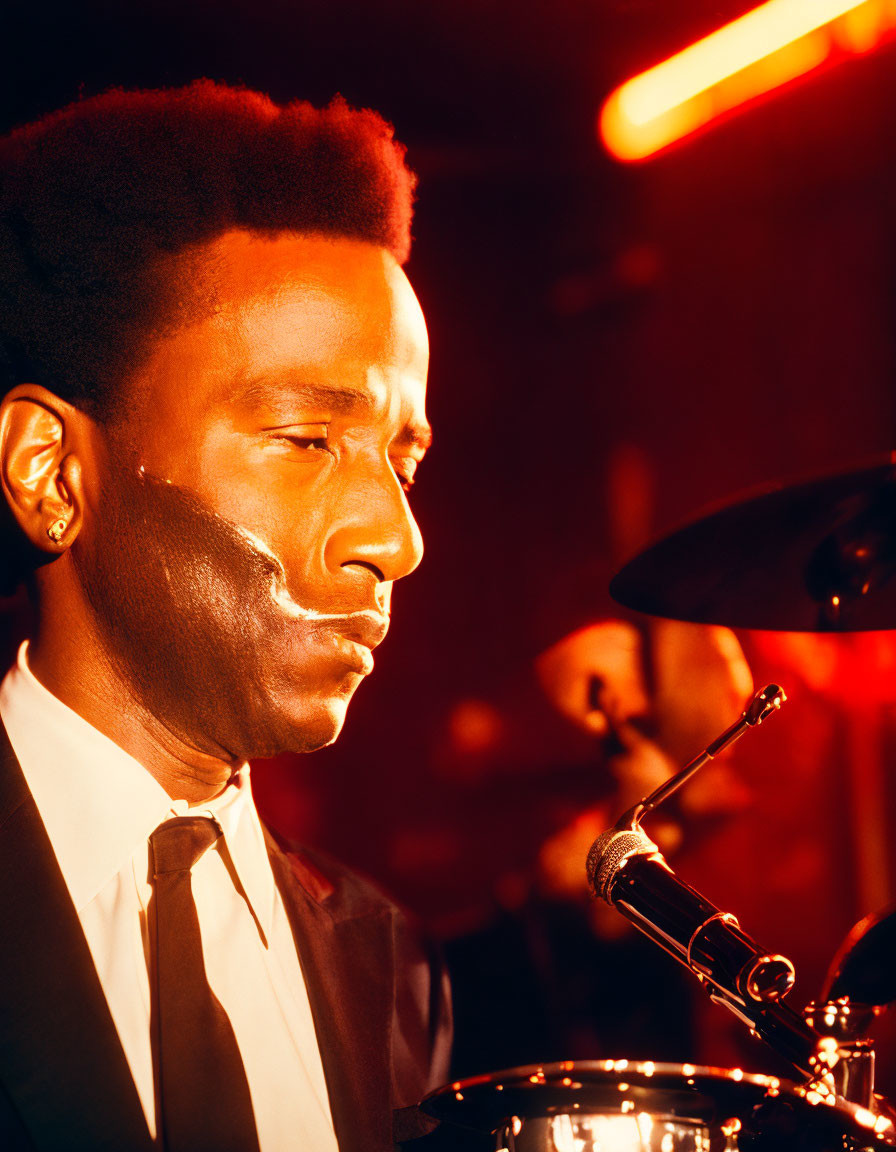 Man in suit playing trumpet on warmly lit stage with out-of-focus drummer