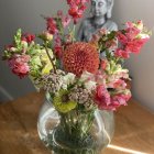 Assorted flowers bouquet in colorful vase on wooden surface