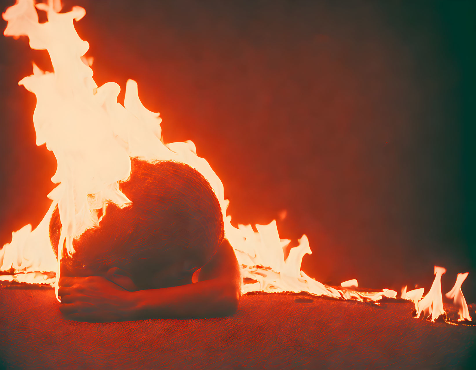 Person in Fetal Position Engulfed in Flames on Dark Background