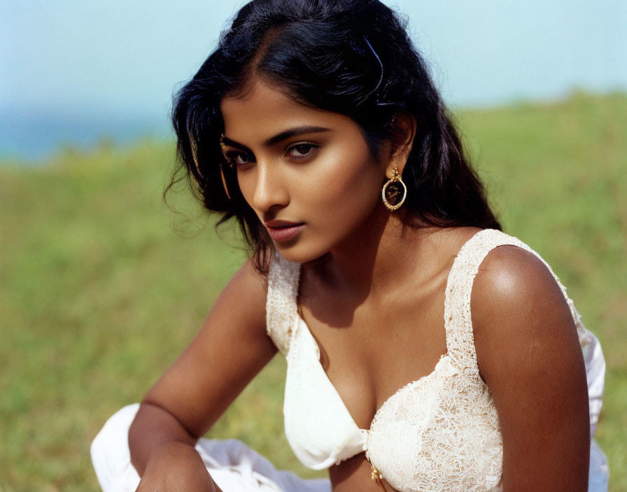 Dark-haired woman in white lace top with earrings, looking sideways in nature setting