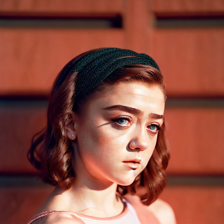 Young woman with headband, intricate hairstyle, and makeup in warm sunlight against wooden background