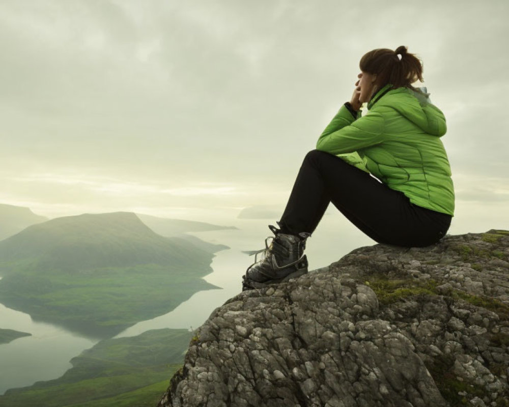 Person in Green Jacket Contemplating Lake View from Rocky Peak