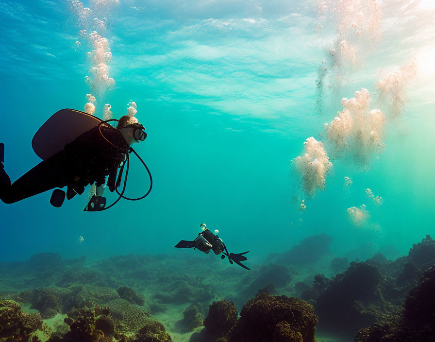 Underwater scuba divers with coral formations and rising bubbles.