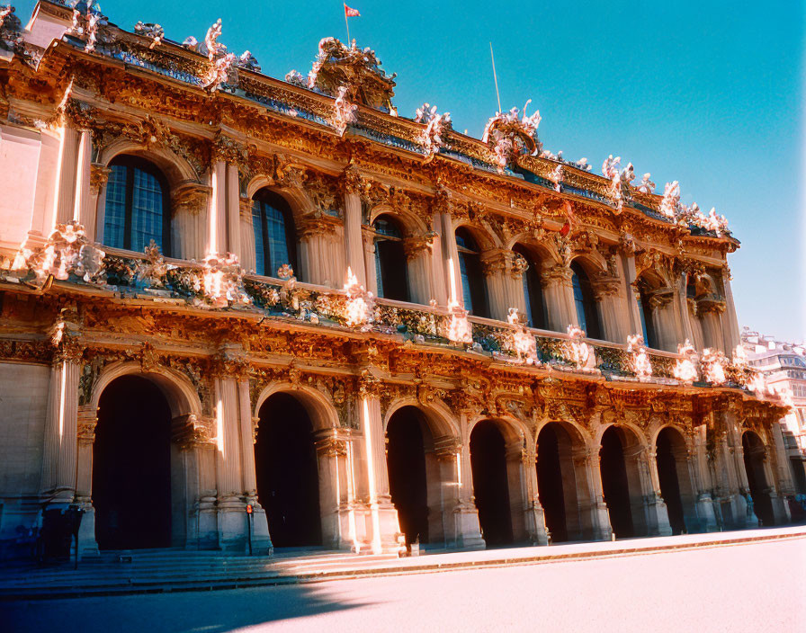 Baroque building facade with archways, sculptures, and flags under blue sky