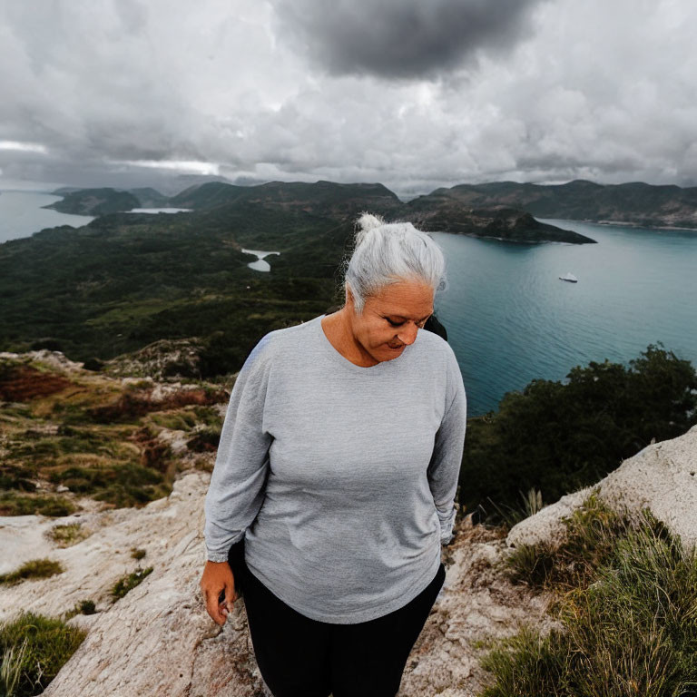 Elderly woman with white hair overlooking seascape on rocky outcrop