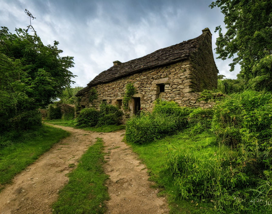 Rustic stone cottage surrounded by greenery on dirt path under cloudy sky