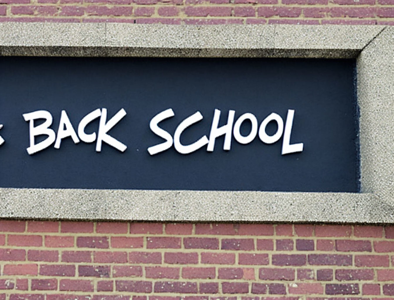 Raised white lettering on black sign against brick wall