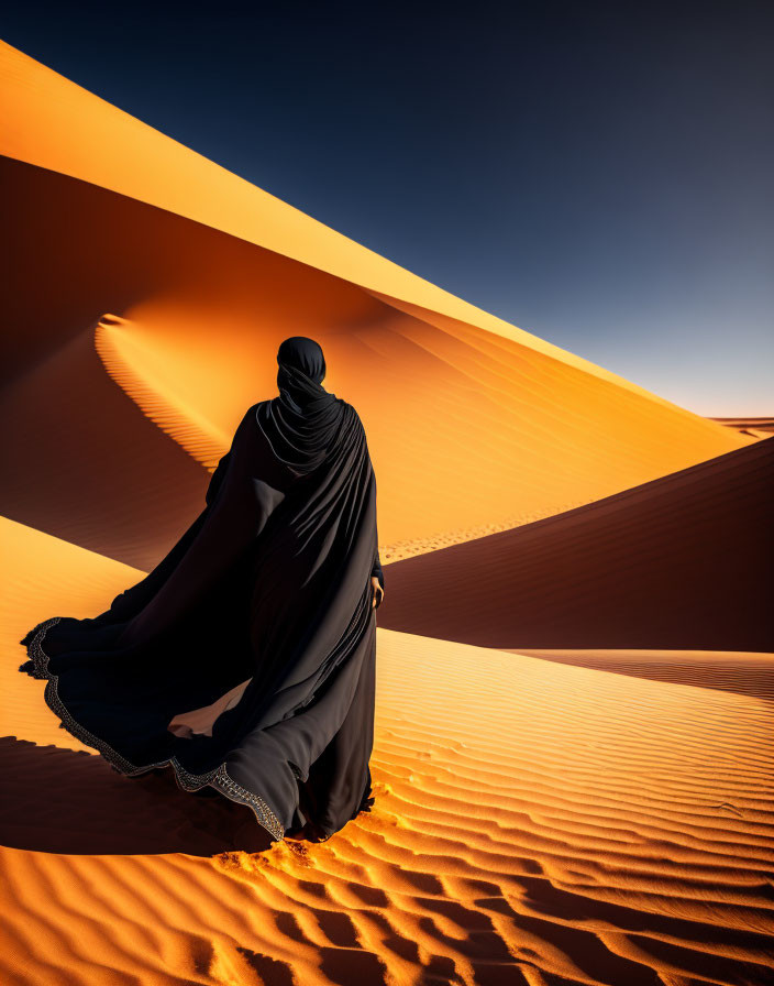 Figure in black cloak on sand dune under clear blue sky