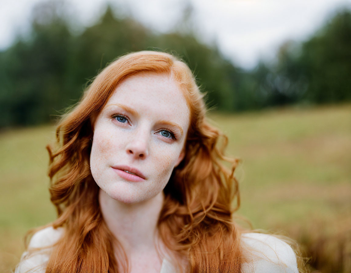 Red-haired woman with freckles in contemplative pose against blurred natural background