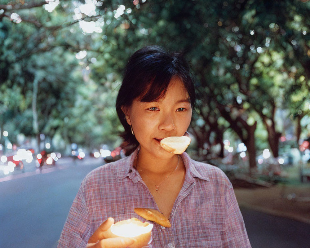 Person with half-eaten snack on tree-lined street with cars