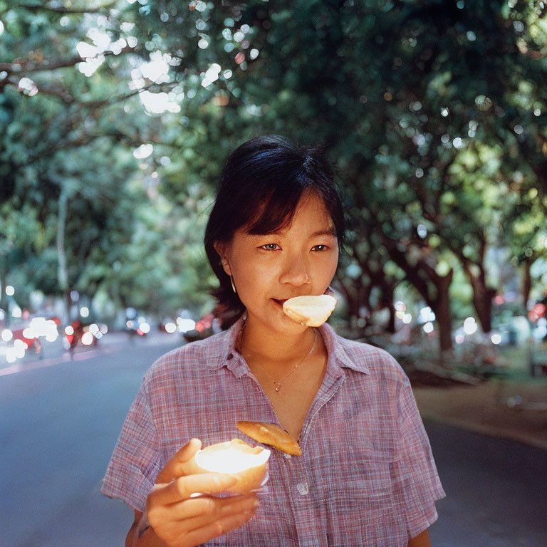 Person with half-eaten snack on tree-lined street with cars