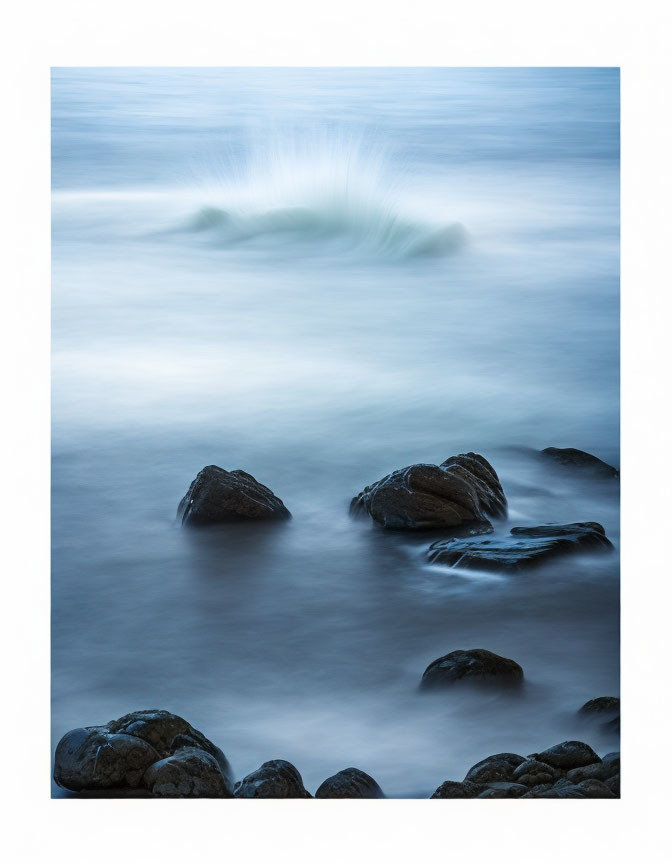 Tranquil seascape with smooth water, dark rocks, and distant wave in shades of blue