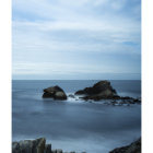 Tranquil seascape with smooth water, dark rocks, and distant wave in shades of blue