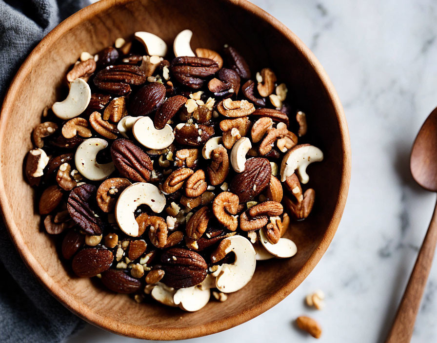 Wooden bowl with almonds, cashews, and pecans on marble surface.