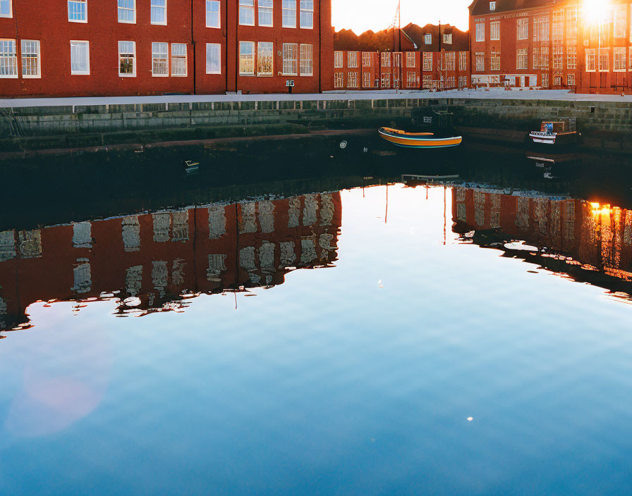 Tranquil water canal with red brick buildings, colorful boat, and dusk sky