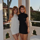 Fashionable women in white and black outfits on balcony with palm trees.