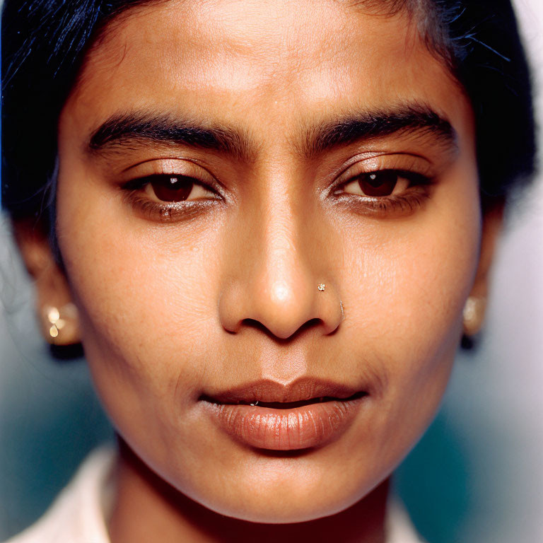 Portrait of person with dark hair and nose piercing on blue background