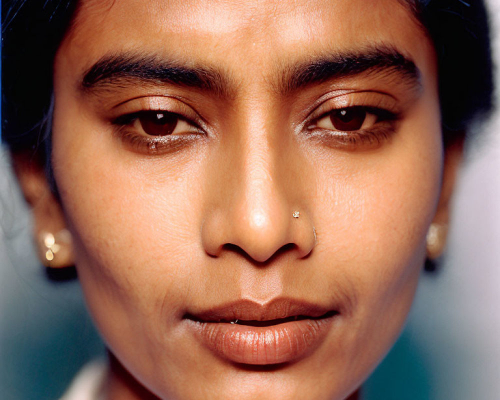 Portrait of person with dark hair and nose piercing on blue background