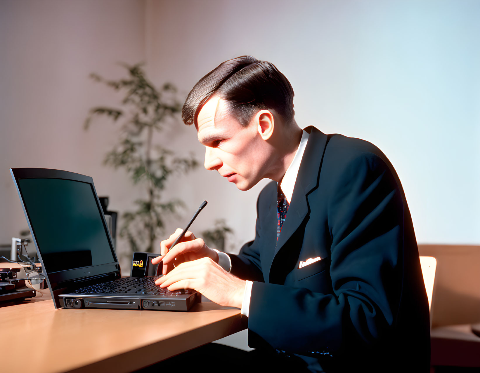 Man in dark suit using laptop and stylus next to antique phone on wooden desk