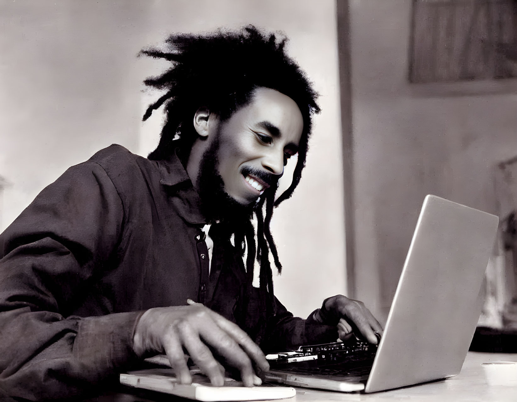 Smiling man with dreadlocks working on laptop in bright room