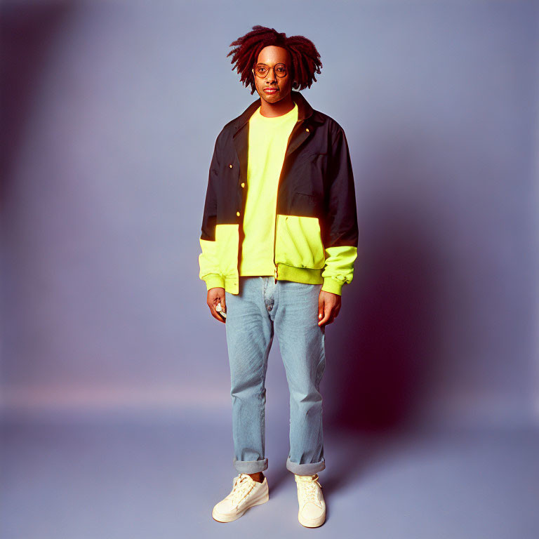 Person with dreadlocks in black and neon jacket, blue jeans, white sneakers on blue background