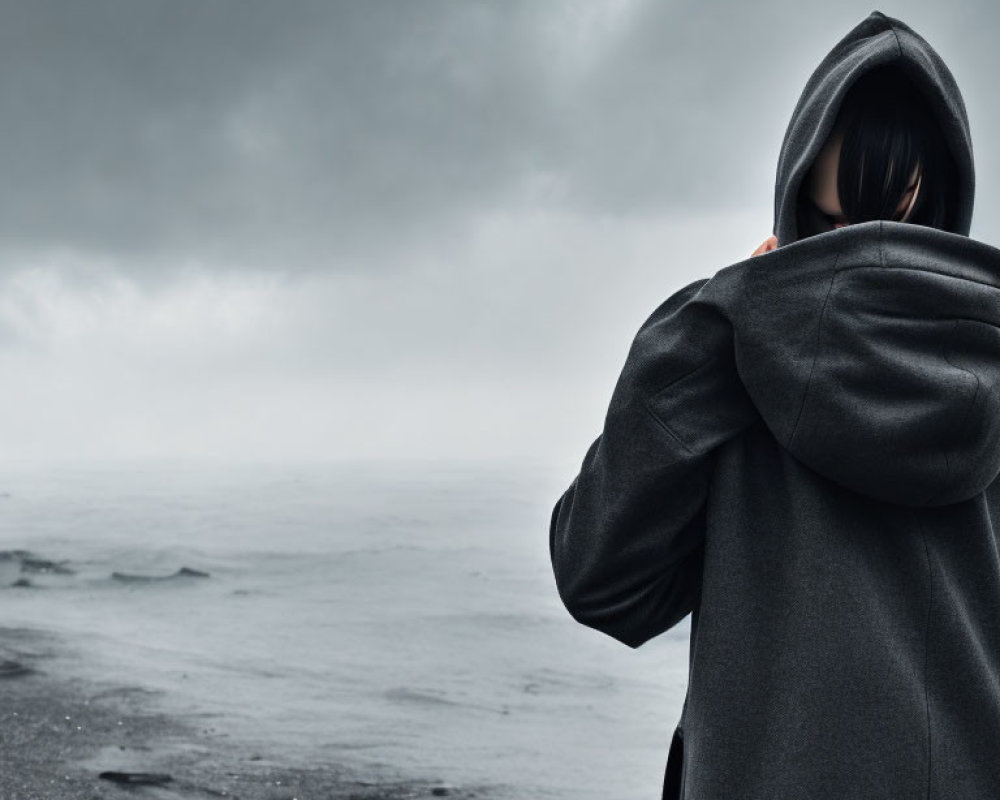 Hooded figure on desolate landscape under overcast sky